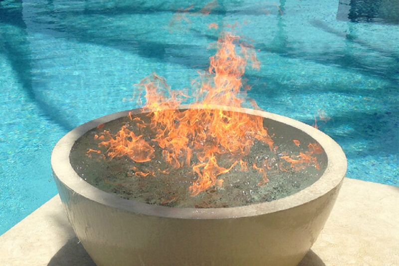 A round gas fire bowl burning at the edge of a swimming pool.