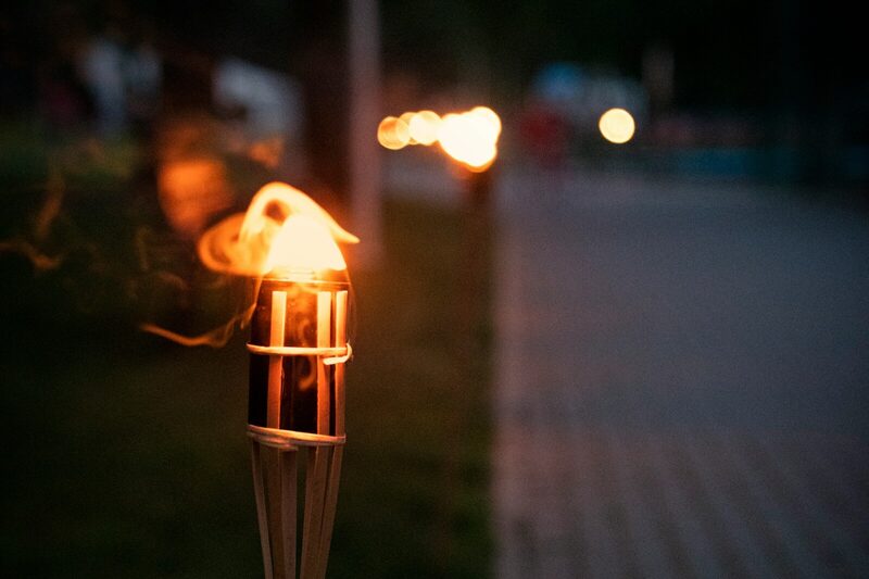 A bamboo tiki torch burning at dusk beside a garden path.