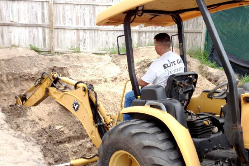 An Elite Gas operator running a backhoe to excavate for a propane tank installation.
