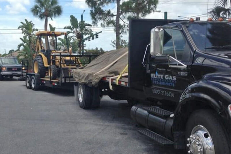An Elite Gas flatbed truck loaded with propane equipment on the road in Palm City, Florida.