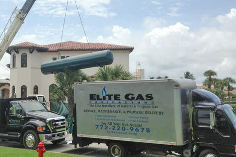 An Elite Gas truck and crane setting a propane tank at a residence.